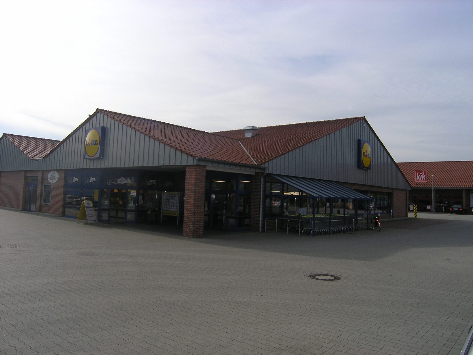 Eingangsbereich mit gläsernem Vordach und Einkaufswagenboxen
